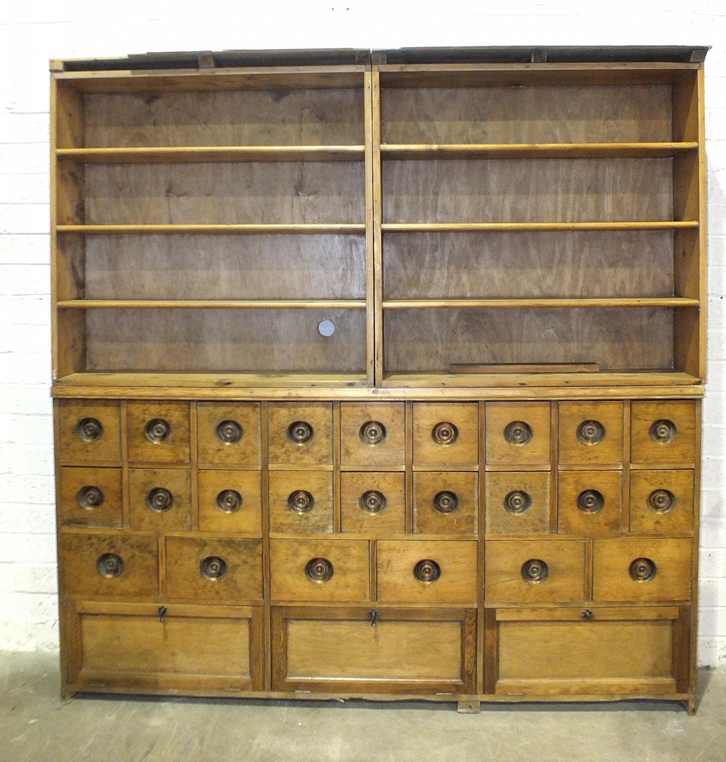 A shop or apothecary's pine cabinet of twenty-four small drawers and three drop-down cupboards,