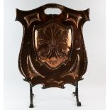 An Arts & Crafts shield form copper fire screen, with hammered decoration, on wrought iron
