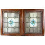 Pair of Arts & Crafts stained glass window panels housed in oak frames, the blue diamond shaped