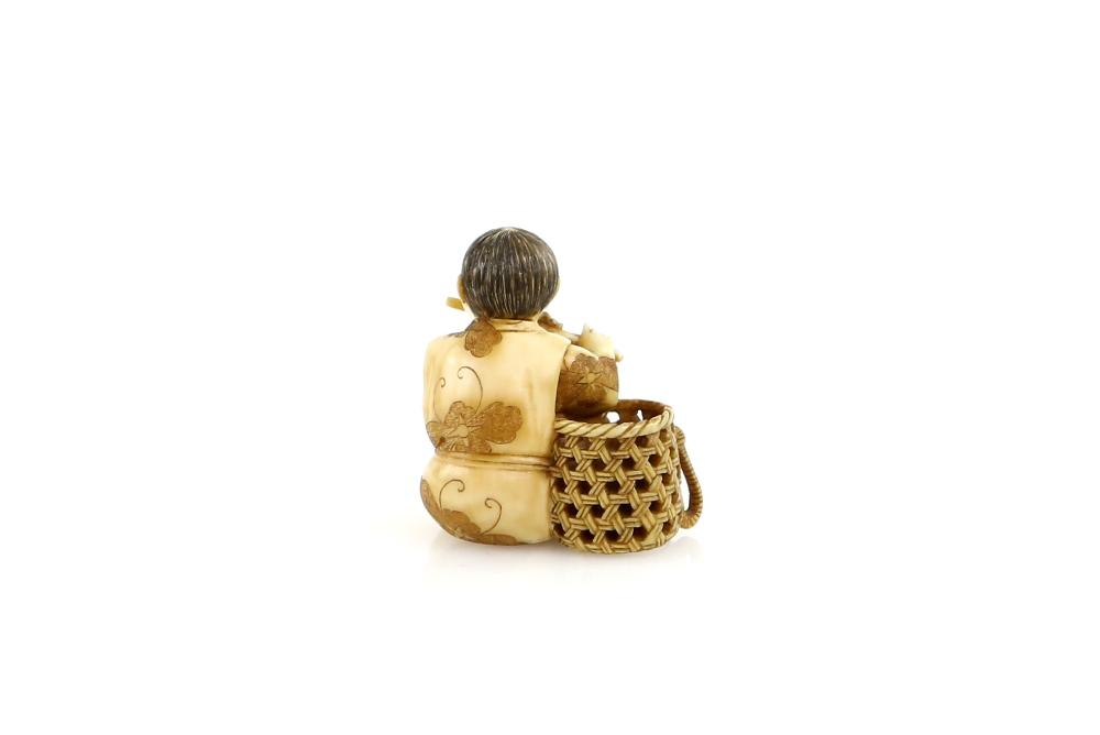 A stained ivory netsuke of a boy flautist, seated beside a basket, signed YoshimitsuProvenance: - Image 2 of 3