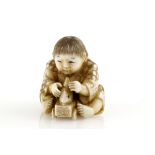 A stained ivory netsuke of a seated boy, playing with a fish toy on wheels, signed