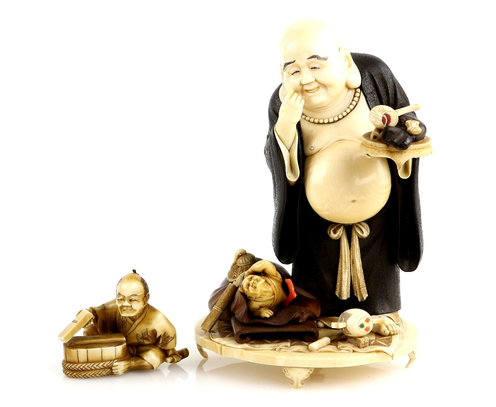 A partially stained ivory okimono, carved as Hotei holding a mallet in his left hand, staring down