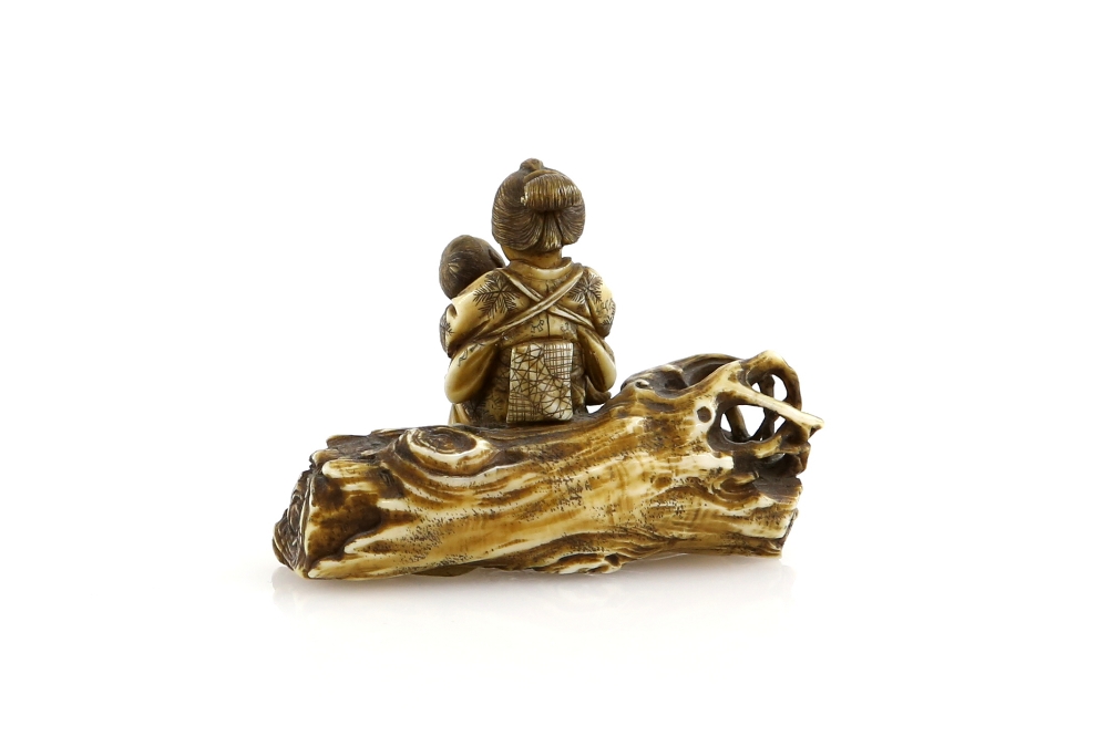 A small stained ivory netsuke or okimono of a mother, seated on a log with her child; two kanji on - Image 2 of 3