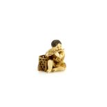 A stained ivory netsuke of a boy flautist, seated beside a basket, signed YoshimitsuProvenance: