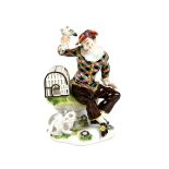 After the Meissen model by J.F. Eberlein, seated figure of a Harlequin teasing a cat with a bird,