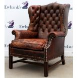 Brown leather button back winged armchair.