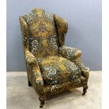 An early 20th C wing back armchair upholstered in Arts & Crafts fabric, on short cabriole legs