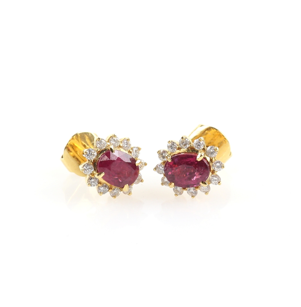 A pair of ruby and diamond earrings, oval faceted stones within a border of diamonds, in unmarked