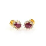 A pair of ruby and diamond earrings, oval faceted stones within a border of diamonds, in unmarked