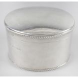 A modern silver caddy, of plain oval form with oblique gadrooned rim to the hinged cover and base.