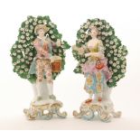 A pair of early 20th Century Continental figures of a lady and gentleman stood before a floral