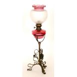 A Victorian oil lamp with ruby reservoir and shade on a brass open work tripod stand,