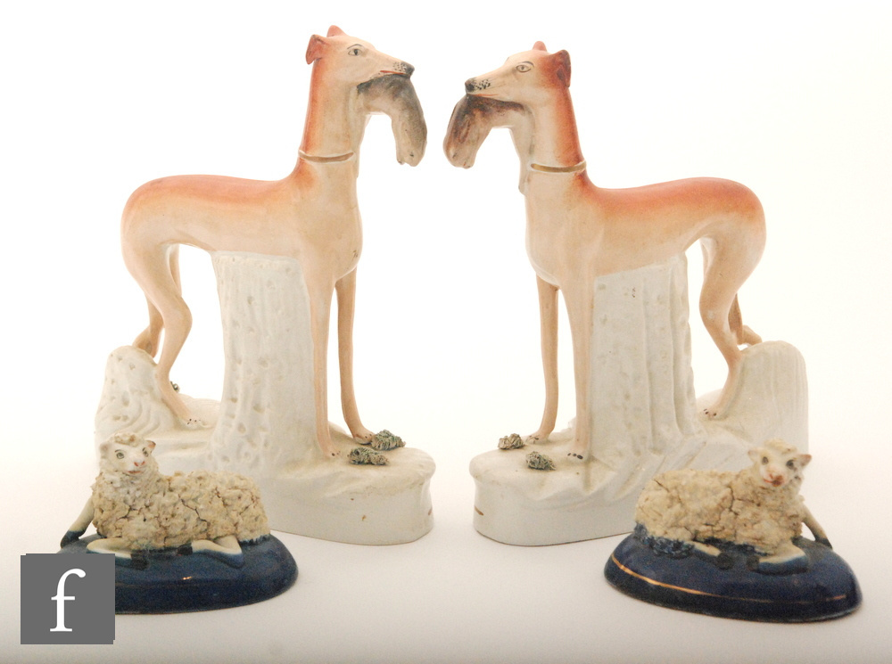 A pair of 19th Century Staffordshire flatback models of whippets stood with rabbits in their mouths