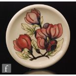 A Moorcroft plate decorated in the Magnolia pattern with three tubelined flowers against a milk