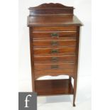 An Edwardian mahogany music cabinet, fitted with five fall-front drawers above a stretcher shelf,