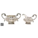 A hallmarked silver cream jug and sugar basin each with embossed foliate decoration around a