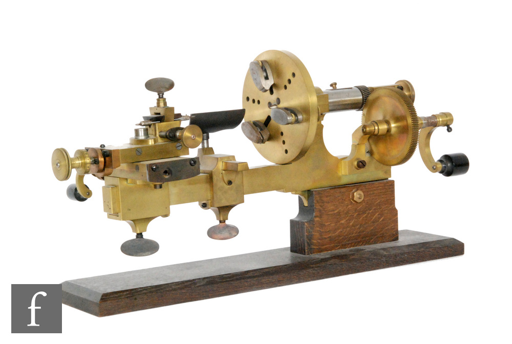 An early 20th Century brass watch makers lathe/mandrel on chamfered oak plinth base, length 46.