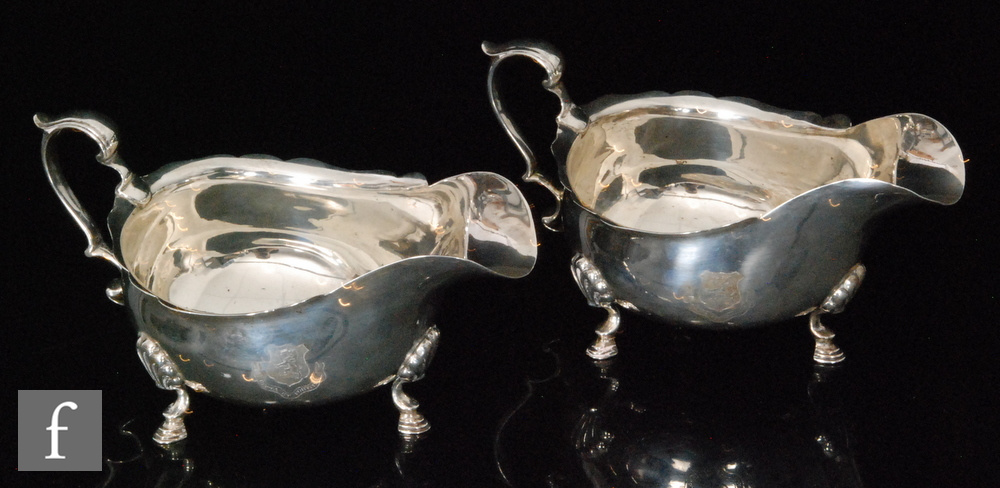 A pair of hallmarked silver sauce boats of plain form each with scroll handle and raised on three