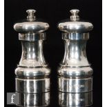 A pair of hallmarked silver pepper mills of typical plain form each terminating in button finial,