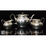 A hallmarked silver three piece boat shaped tea set of plain form with shaped borders and scroll