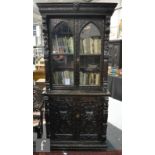 A Victorian carved dark oak bookcase enclosed by a pair of arched glazed doors below a cornice