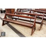 A pair of stained pine pews each with iron bar supports and book shelf on shaped open ends, height