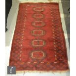 An Afghan rug with a central row of six guls on a red ground within a geometric border, 183cm x