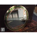 An Art Deco bevelled glass wall mirror of circular form, with green and peach coloured borders,