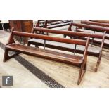 A pair of stained pine pews each with iron bar supports and book shelf on shaped open ends, height