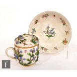 A late 19th to early 20th Century Dresden type custard cup and saucer, both decorated with applied