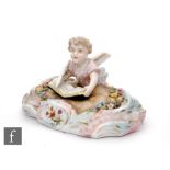 A 19th Century continental hard paste porcelain figure modelled as a resting cherub writing to a