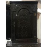 A Victorian carved dark oak hanging corner cupboard enclosed by an arch and fan inlaid door below