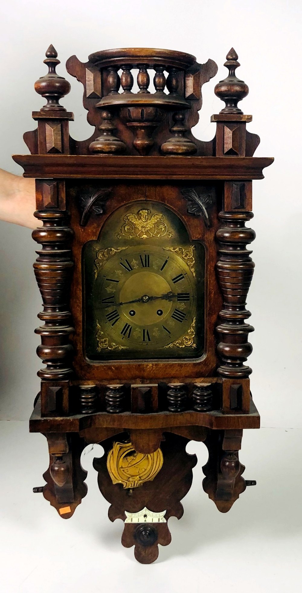 A walnut carved Vienna Wall Wagger, with small arched brass face and brass pendulum,
