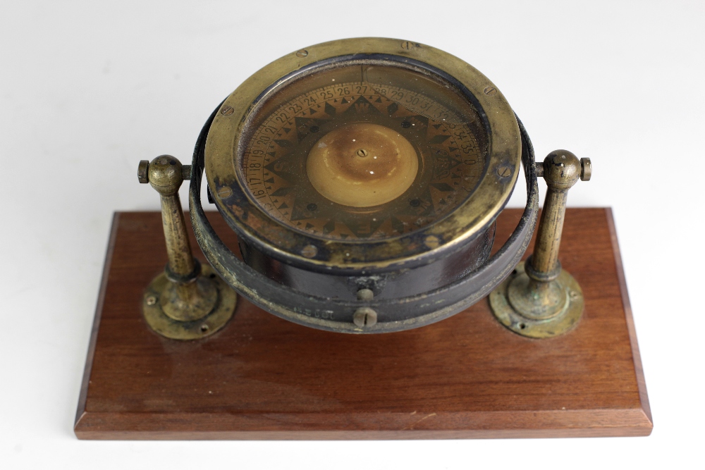 An early 20th Century brass Ships Compass, with rotating dial mounted on a wooden platform base.