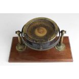 An early 20th Century brass Ships Compass, with rotating dial mounted on a wooden platform base.