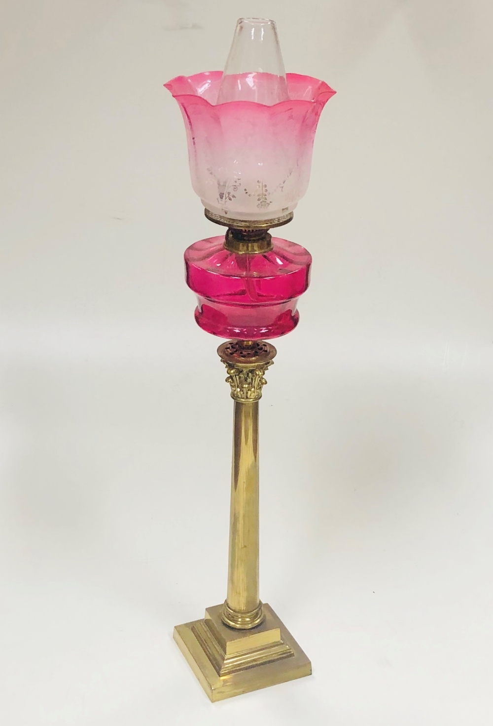 A tall antique brass Corinthian style Table Lamp, with crimson glass bowl, plain glass globe,