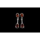 Red Garnet Drop Earrings, a pear cut red garnet suspended below a round cut, by a shaped silver bar,