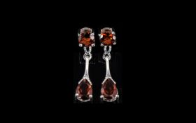 Red Garnet Drop Earrings, a pear cut red garnet suspended below a round cut, by a shaped silver bar,