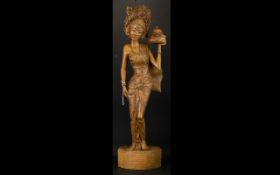 A Carved Wood Balinese Figure In the form of a maiden in traditional sarong and headdress,