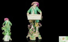 Chelsea Hand Painted Porcelain Figure of a Bare Footed Young Man Carrying a Large Empty Basket,