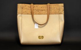 Fashion Tote Bag in gold with cork trim and tan leather handles. Gold badge to front.