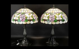 A Pair Of Reproduction Tiffany Style Table Lamps each raised on bronzed metal base with shaped