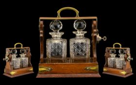 An Early Twentieth Century Oak Cased Two Bottle Tantalus with brass Gothic strap work and locking
