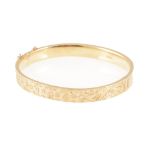 A 9 carat yellow gold hollow half hinged bangle, 8mm wide flat section with a floral engraved
