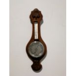 A small oak cased aneroid wall barometer with thermometer, carved detail to top and bottom, overall