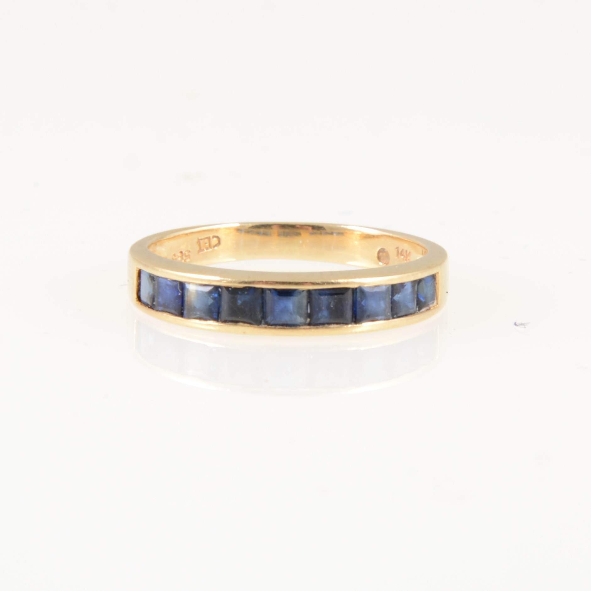 A sapphire half eternity ring, nine square cut stones channel set in an all yellow metal mount,
