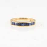 A sapphire half eternity ring, nine square cut stones channel set in an all yellow metal mount,