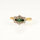 An emerald and diamond cluster ring, three small emeralds claw set horizontally and surrounded by