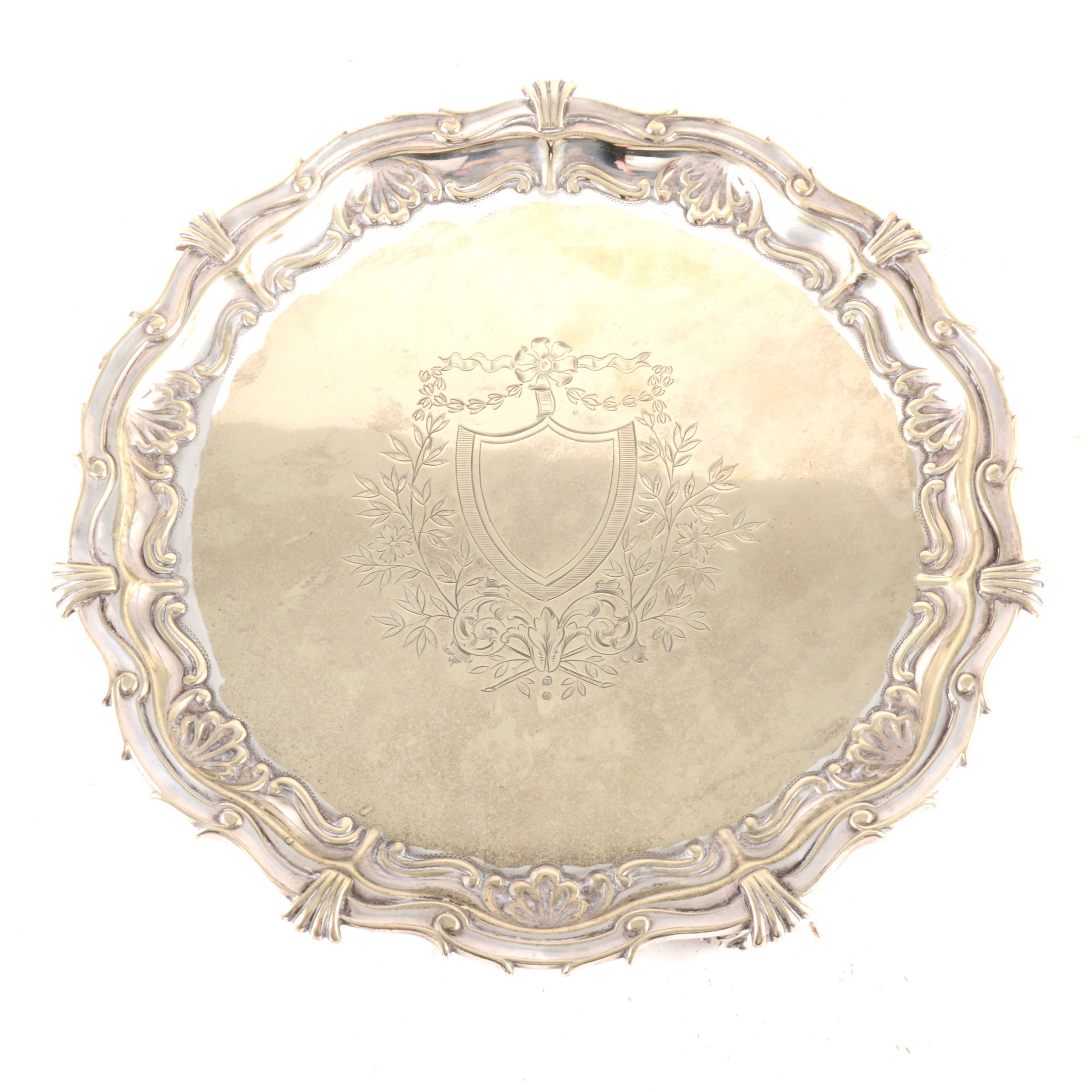 A silver-plated salver with shield to centre, shell border on three cast scroll feet.