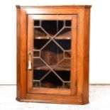 A Victorian elm hanging corner cupboard, with glazed panelled door enclosing serpentine shelves,